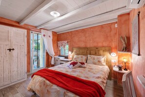 Un dormitorio con cama, mesita de noche, ventana con cortinas, cabecera de madera y puerta.