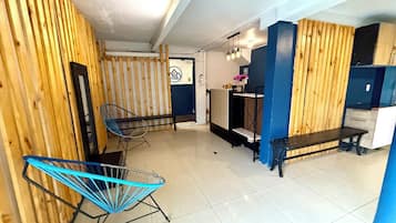 Una habitación con pared de listones de madera, una silla azul, un banco y una pequeña cocina.