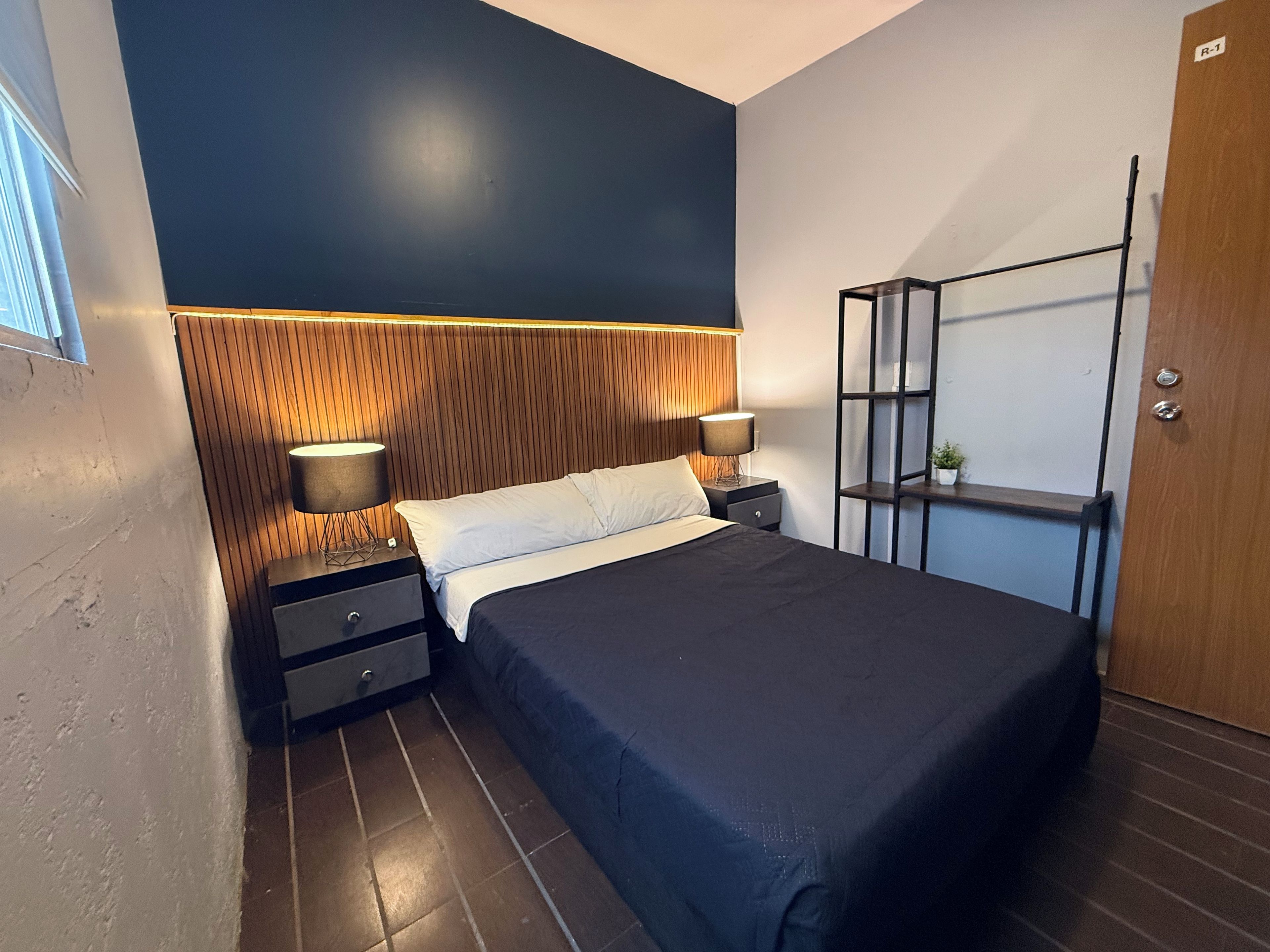Camera da letto moderna con un letto, due comodini con lampade, una testiera in legno, una mensola a incasso e una porta.