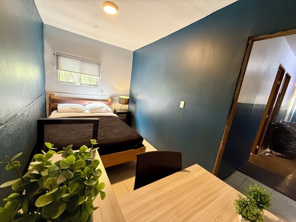Una habitación pequeña con cama, una mesita y una planta en maceta.
