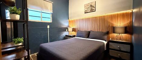 Un dormitorio moderno con una cama grande, mesitas de noche, una mesita auxiliar, una ventana con vistas y un cuadro colgado en la pared.