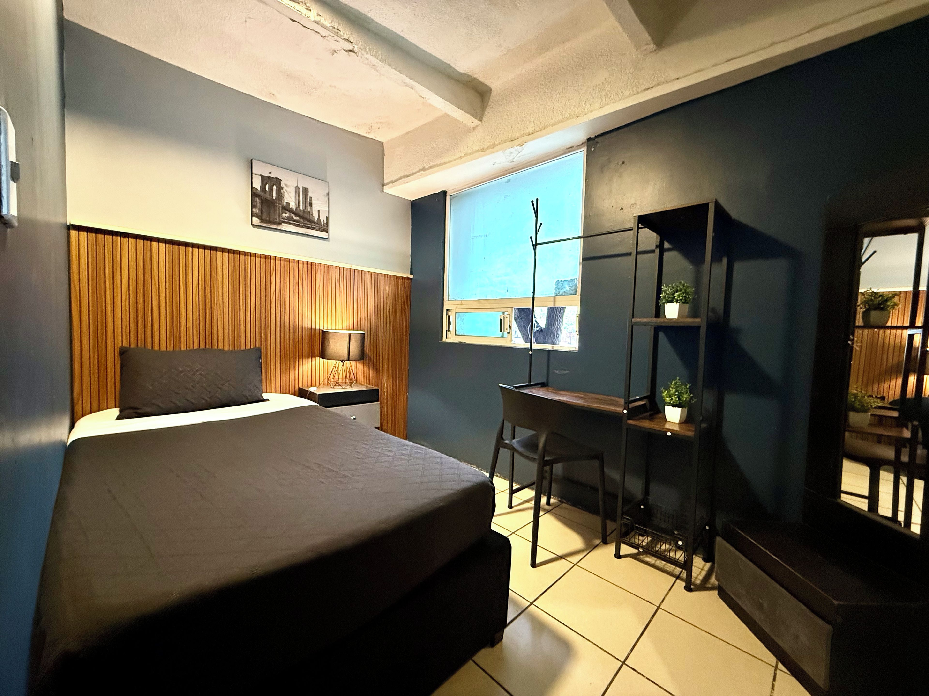 Quarto com cama, escrivaninha, cadeira, janela e espelho.