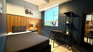 Quarto com cama, escrivaninha, cadeira, janela e espelho.