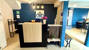 Un mostrador de recepción con una pared azul, una pequeña maqueta de una casa y un cartel que dice 'ROOMIES'.