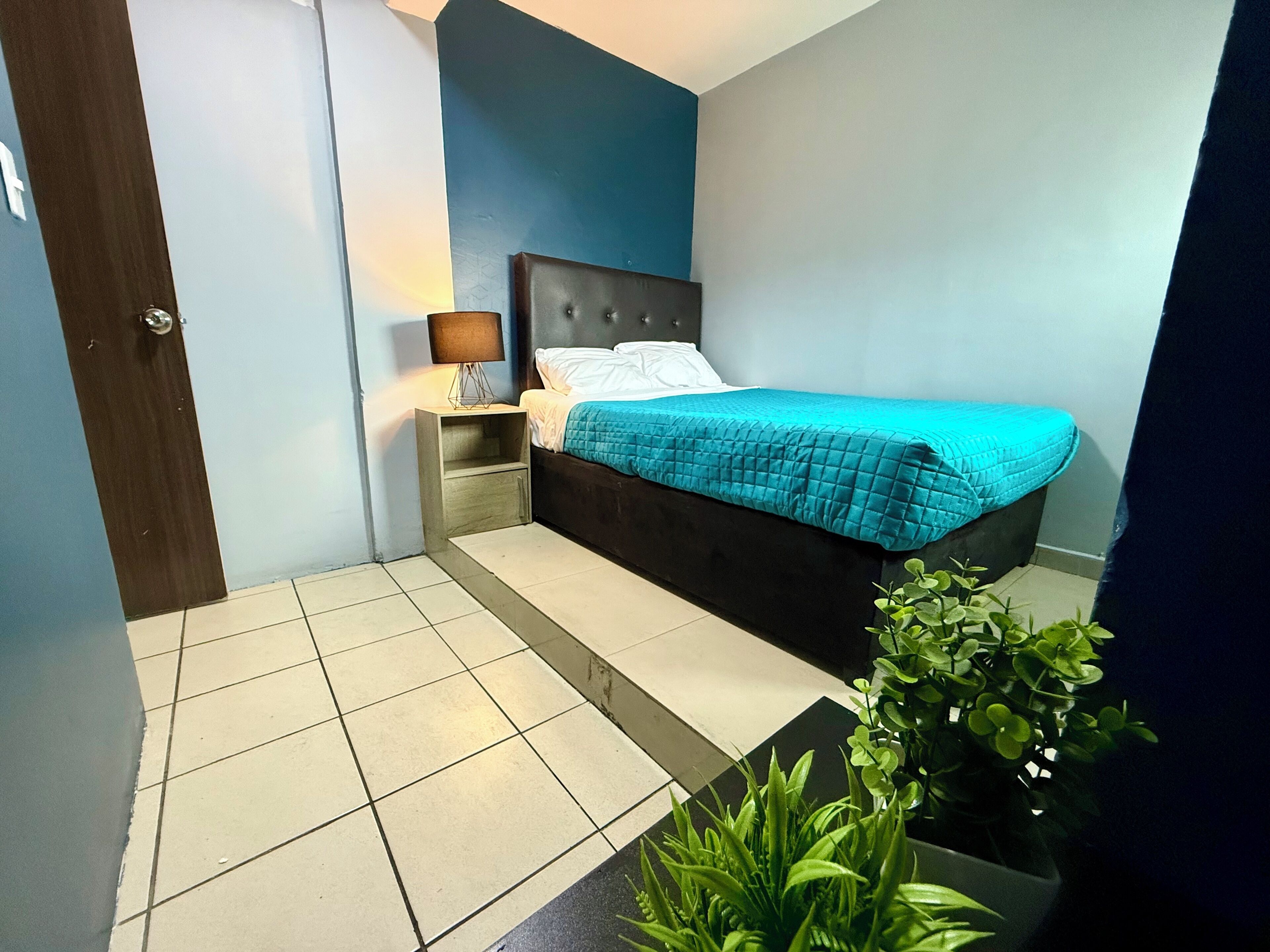 Un dormitorio con cama, mesita de noche, lámpara y planta en maceta.