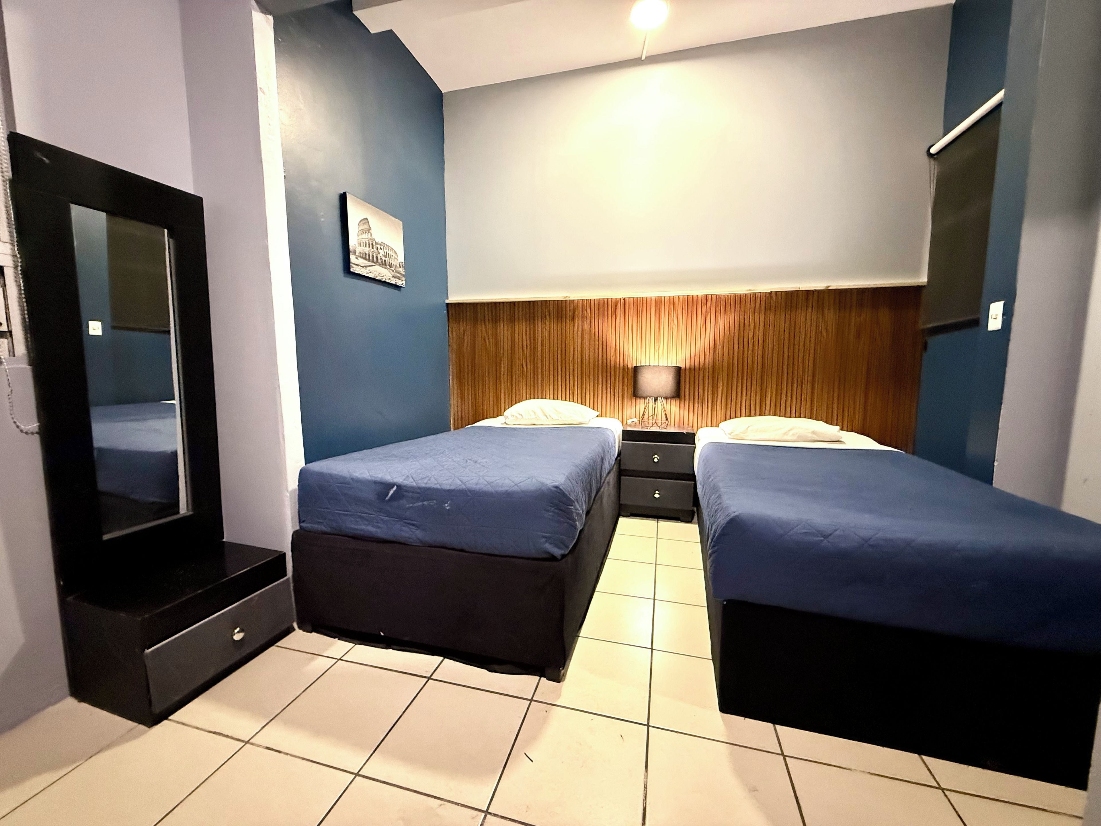 A hotel room with two beds, a large mirror, a wooden headboard, a nightstand, and a wall-mounted TV.