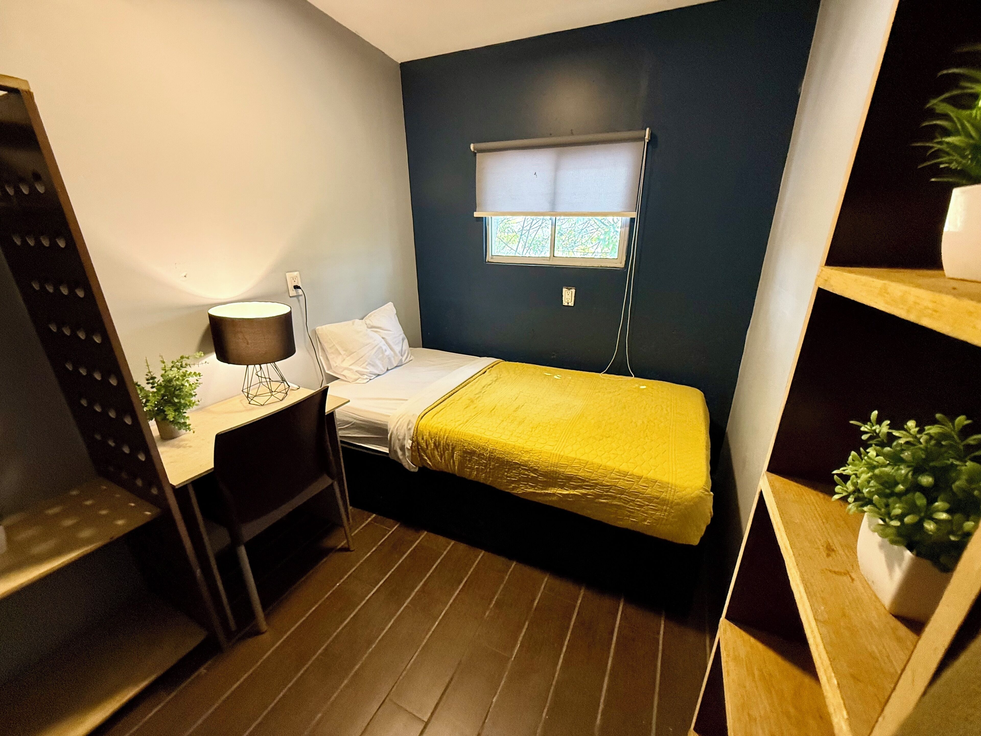 Una habitación pequeña y funcional con cama, escritorio y ventana.