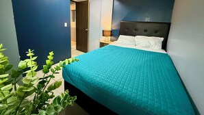 A modern bedroom with a large bed, a dark headboard, and a blue accent wall. - RHM Spaces - Santa Maria (Mexico City)