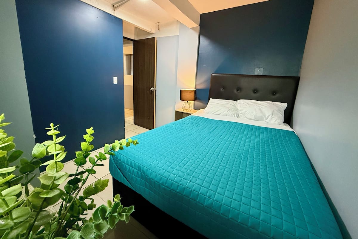 A modern bedroom with a large bed, a dark headboard, and a blue accent wall.
