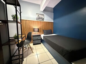 Ein Schlafzimmer mit einem Bett, einem Schreibtisch, einem Stuhl, einem Nachttisch und einem an der Wand befestigten Fernseher.