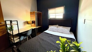 A compact bedroom with a bed, a desk, and a chair. There is a window providing natural light. - RHM Spaces - Santa Maria (Mexico City)