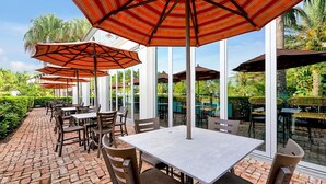 An outdoor patio with brick flooring, tables, chairs, and striped umbrellas.