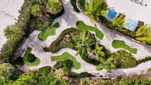 An aerial view of a landscaped area with winding pathways, green lawns, and a pool.