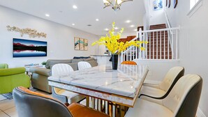 A modern dining area with a marble table, white chairs, and a vase of yellow flowers.