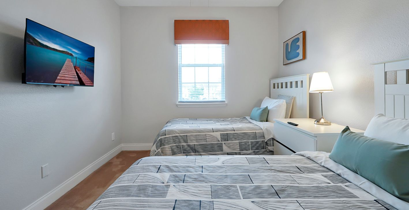 Una habitación individual con dos camas, un televisor inteligente montado en la pared, una ventana con persianas, un ventilador de techo y una lámpara de noche.