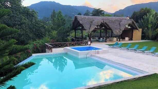 Zona de piscina amb una piscina blava cristal·lina, gandules i una estructura amb teulada de palla.