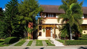 Una casa de dues plantes amb teulada de rajola, un porxo i un jardí ben cuidat amb diversos arbres i arbustos.