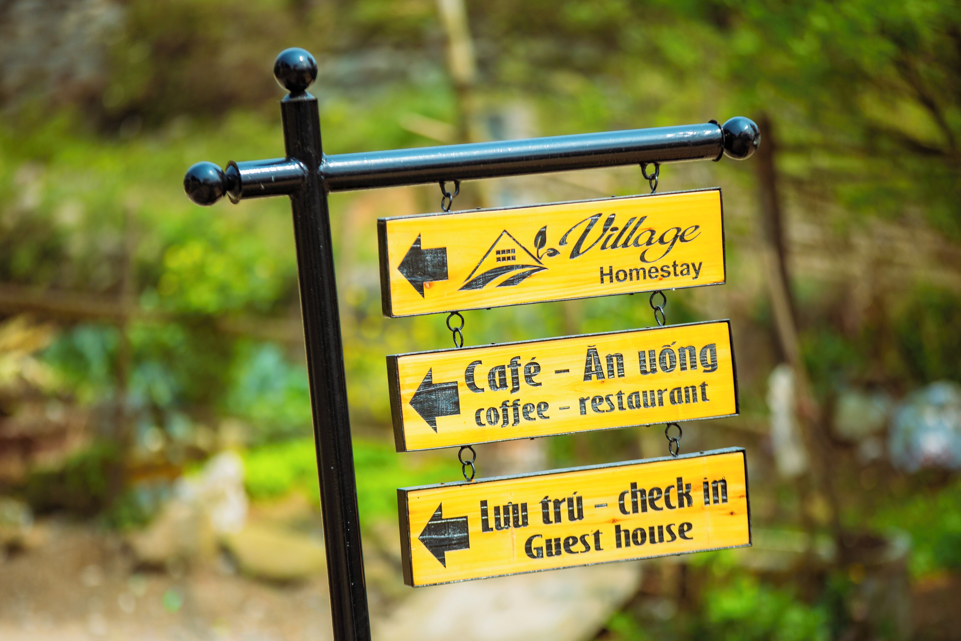 Un panneau indicateur avec des flèches et du texte indiquant la direction d’un village proposant des hébergements chez l’habitant, d’un café et d’une maison d’hôtes.