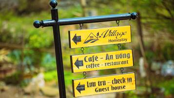 Un panneau indicateur avec des flèches et du texte indiquant la direction d’un village proposant des hébergements chez l’habitant, d’un café et d’une maison d’hôtes.