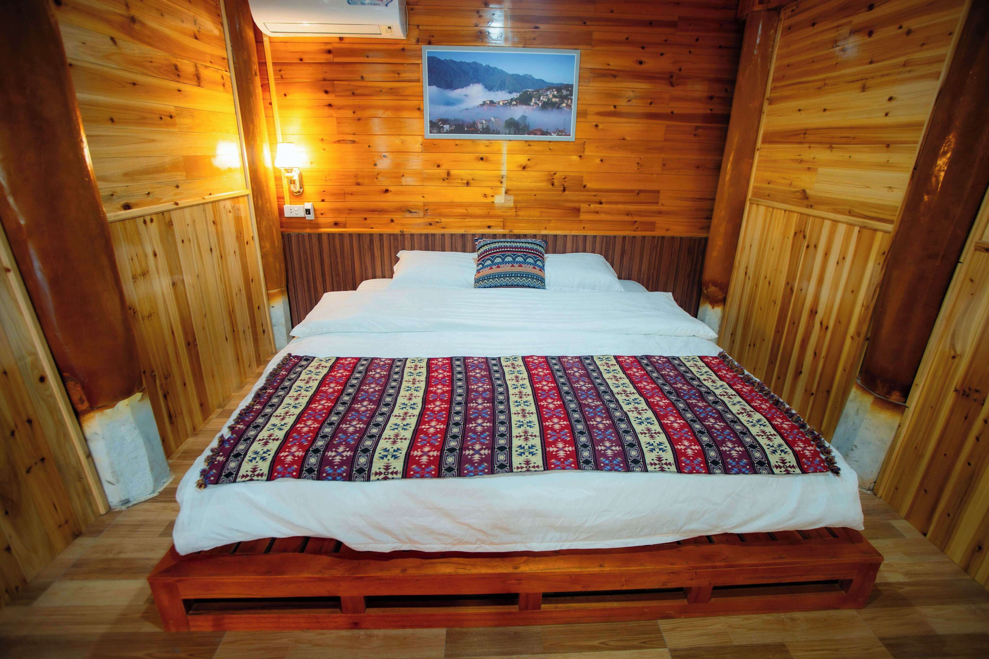 Une chambre rustique en bois, avec un lit, un tableau encadré au mur et une petite lampe de chevet.