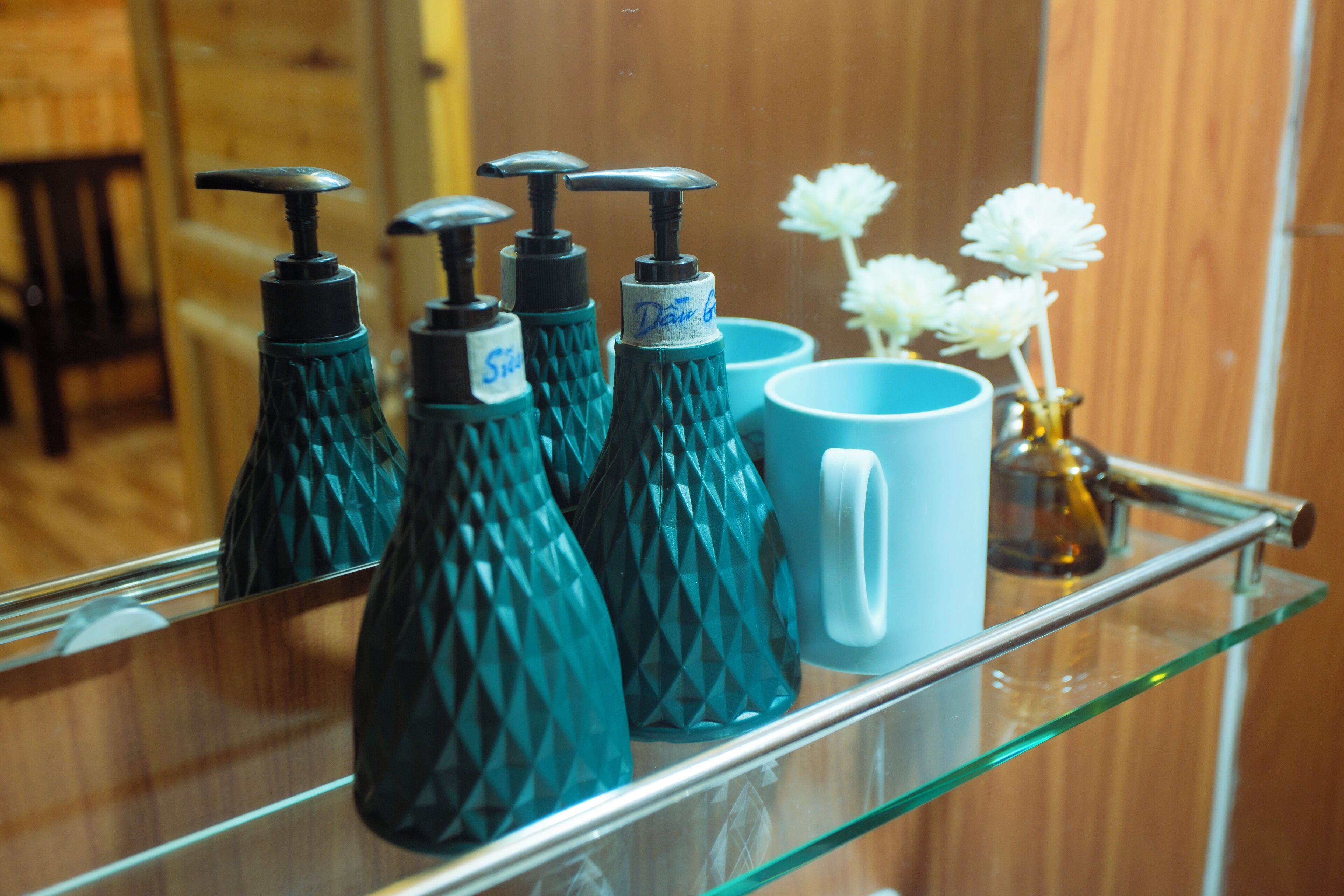 Uma prateleira de vidro com dosadores de sabonete azul-turquesa e uma caneca azul.