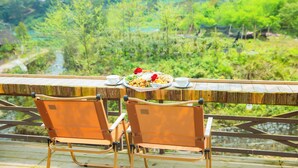 A dining table with a plate of food and two chairs, overlooking a lush green landscape with a river and houses in the background. - SaPa Village Retreat - Dine & Coffee (Sa Pa)