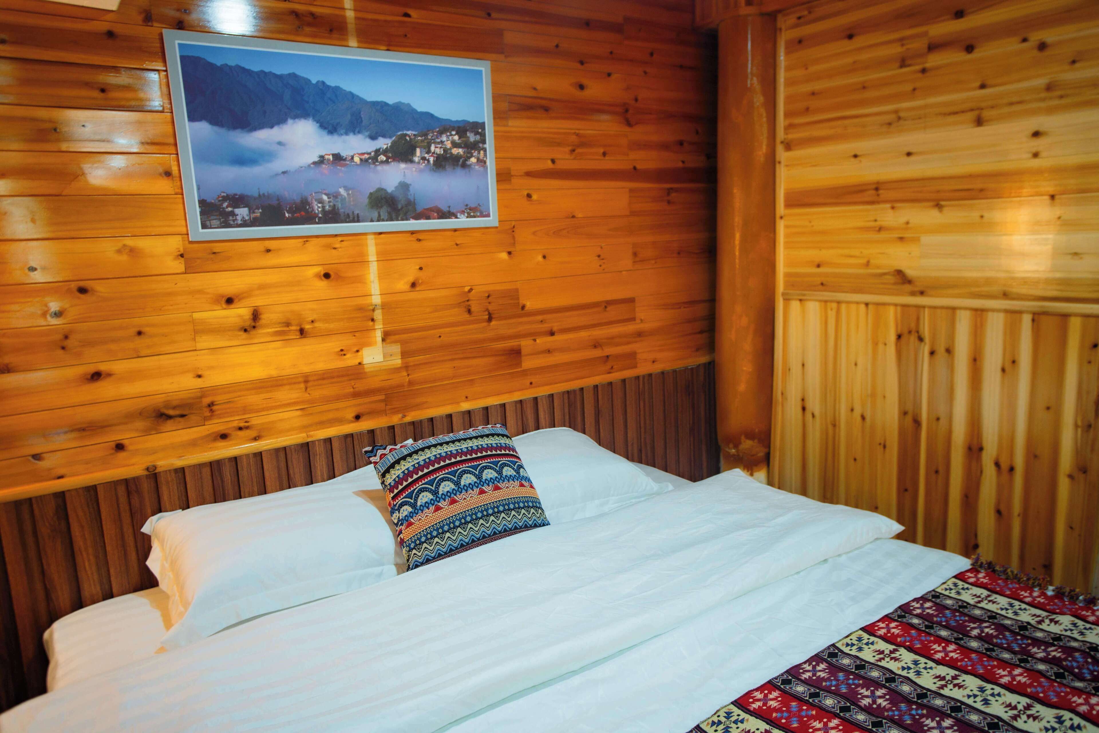 Um quarto de cabana de madeira com uma cama, um quadro na parede e um cobertor estampado.