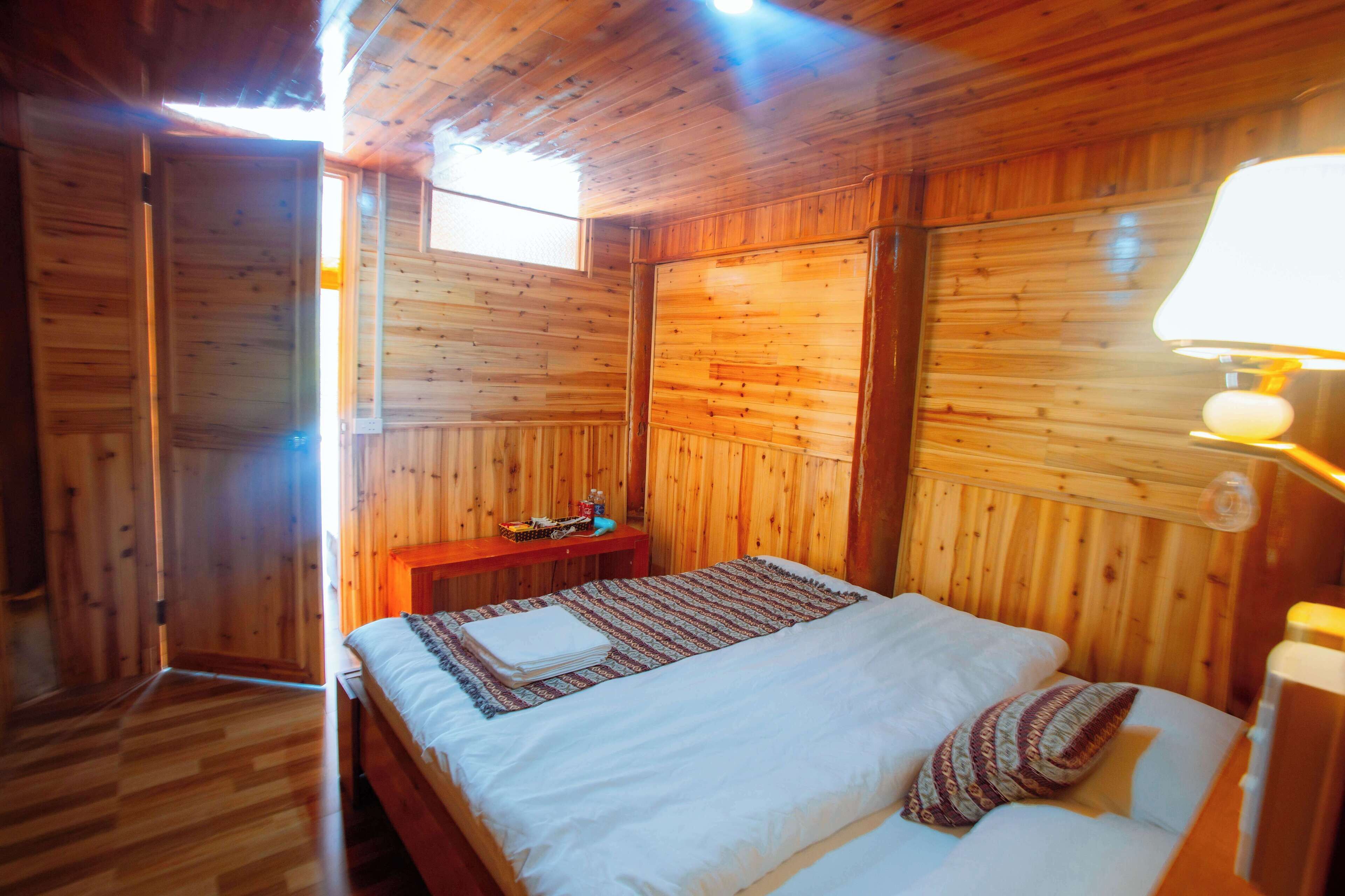 A wooden room with a bed, a nightstand, and a window.