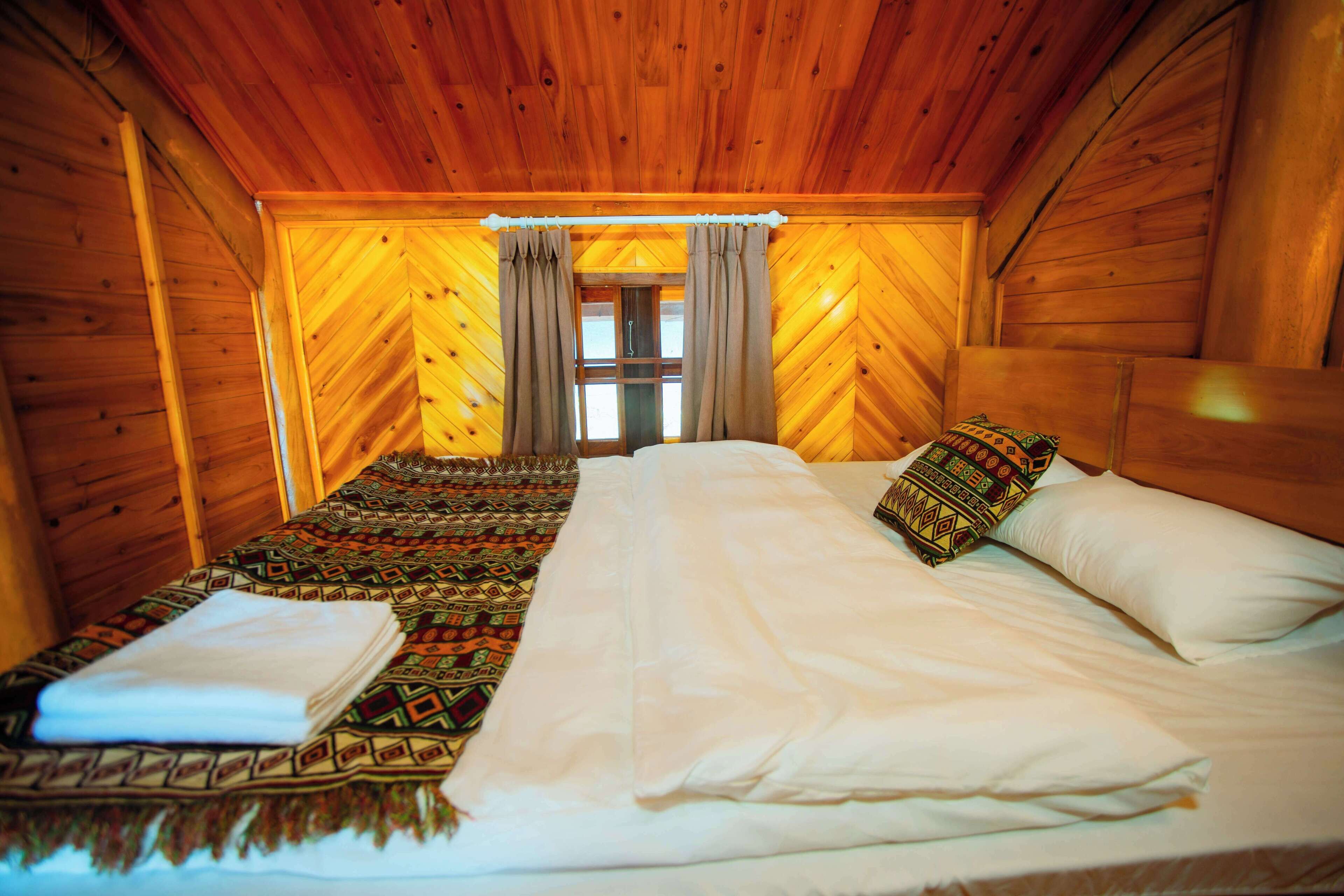 Une chambre de chalet en bois avec deux lits, une couverture à motifs et une fenêtre avec des rideaux.