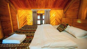 Une chambre de chalet en bois avec deux lits, une couverture à motifs et une fenêtre avec des rideaux.