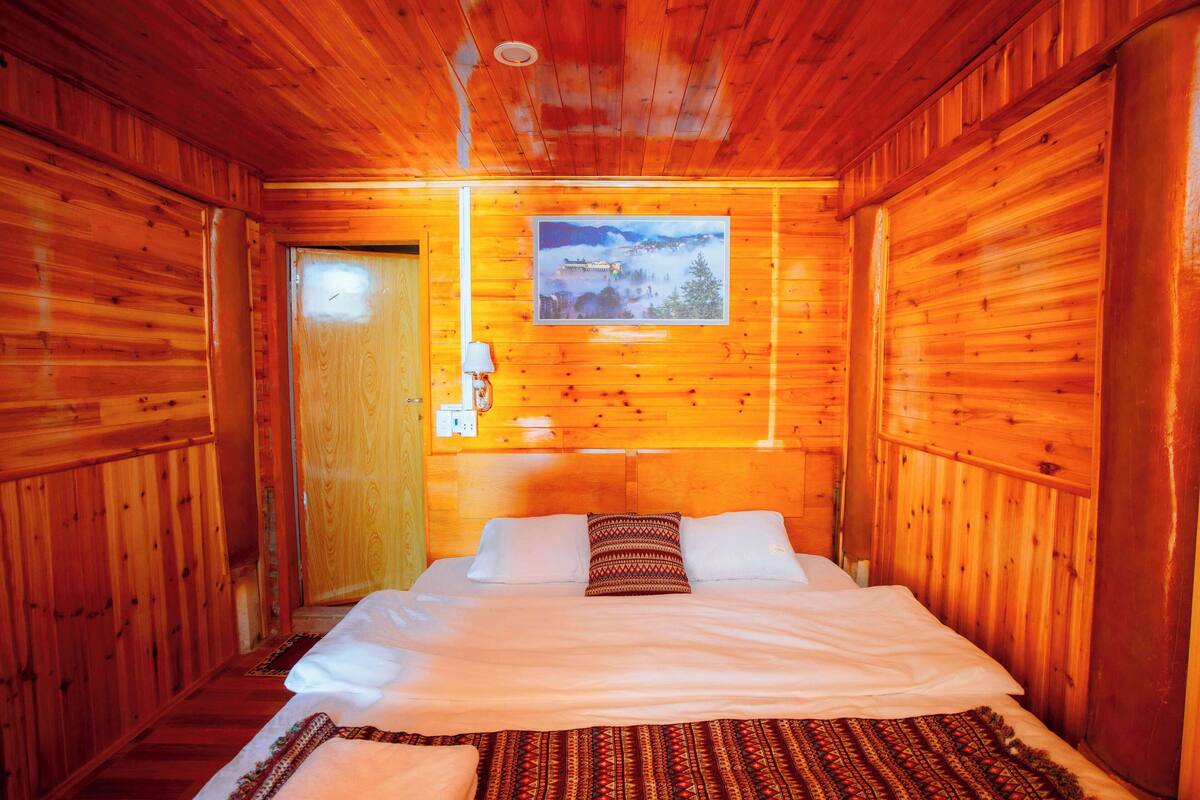 Ein Zimmer in einer Holzhütte mit einem Bett, einem Bild an der Wand und einer Holztür.