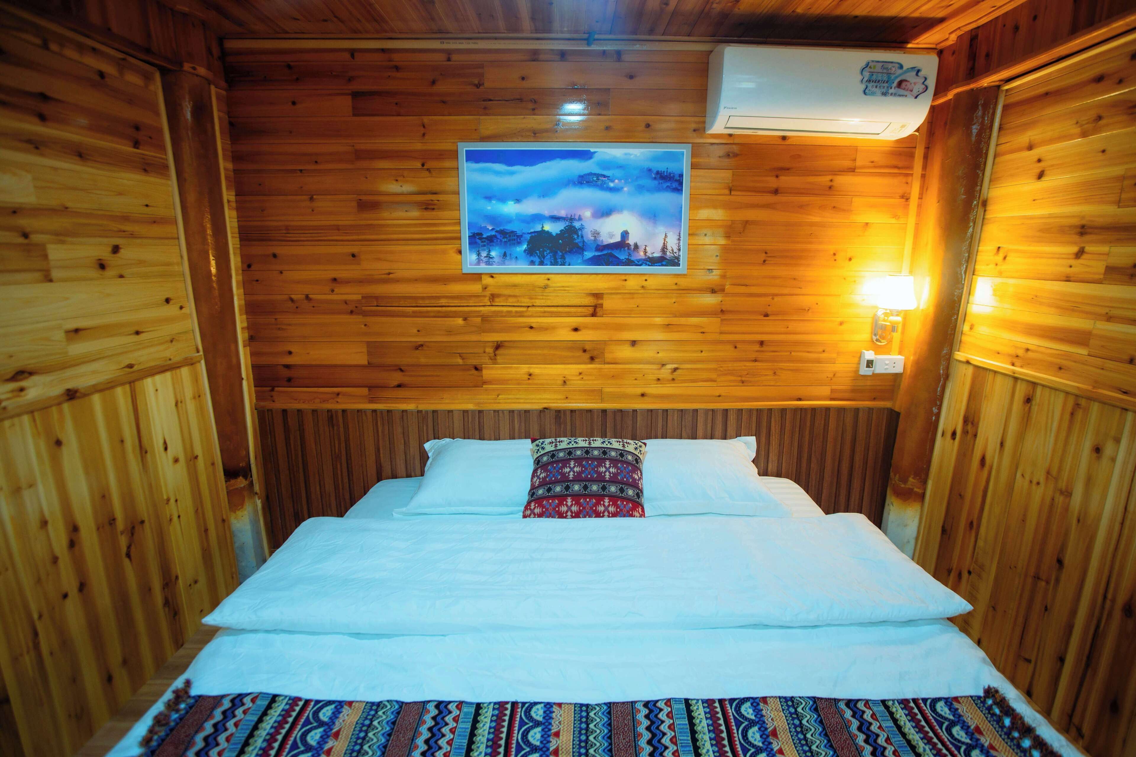 Une chambre dans un chalet en bois, avec un lit, un climatiseur fixé au mur et un tableau encadré au-dessus du lit.