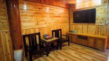 A wooden-paneled room with a television mounted on the wall, a bench, and a small table with items on it.