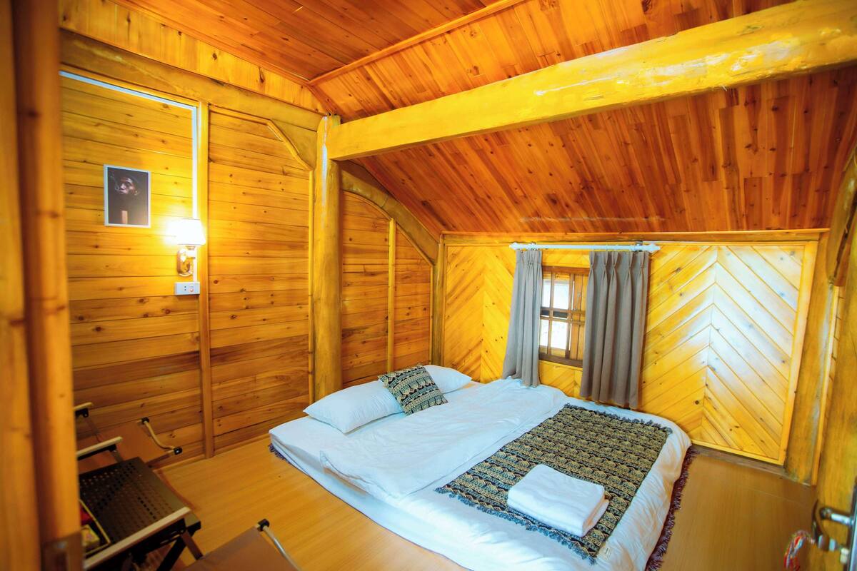 Ein Zimmer in einer Holzhütte mit einem Bett, einem Schreibtisch und einem Fenster mit Vorhängen.