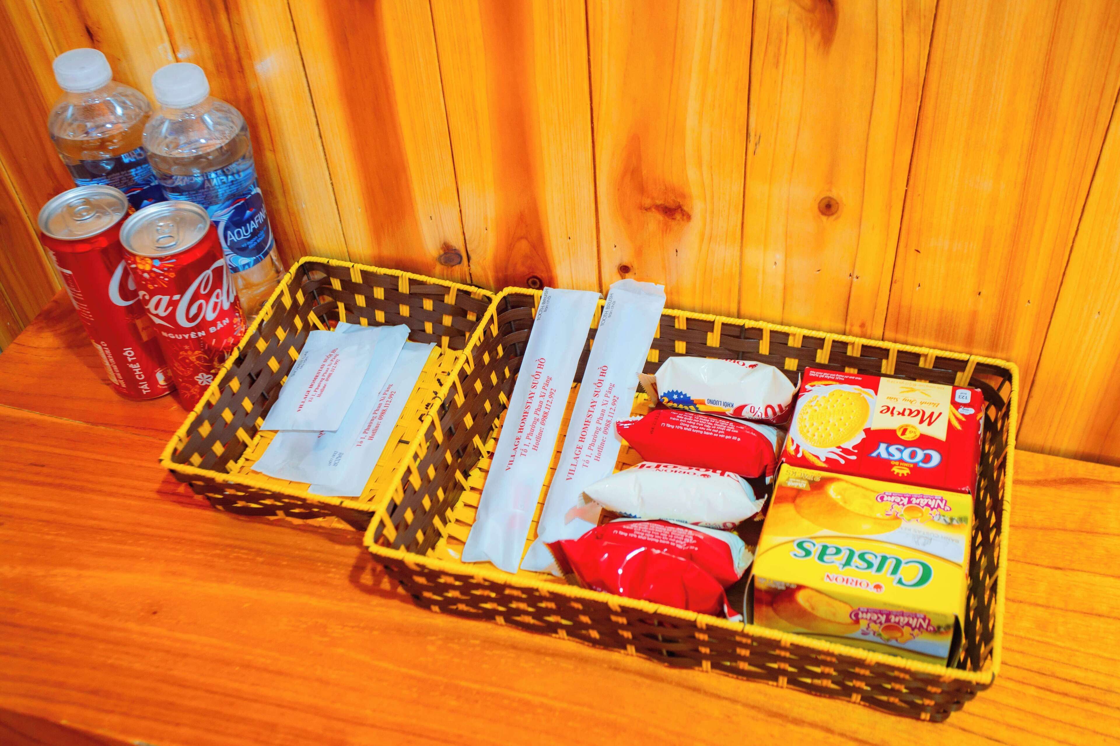 A wooden table with a basket containing snacks, a bottle of Coca-Cola, and a bottle of Aquafina water.