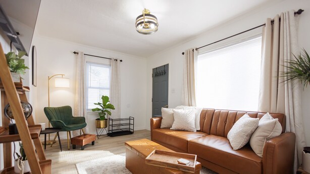Una sala de estar moderna con un sofá de cuero marrón, una mesa de centro de madera, un sillón verde y una lámpara de pie.