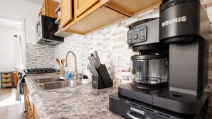 Una cocina moderna con una cafetera Keurig, encimera de granito y armarios de madera.