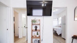 Un pasillo con un estante de madera, un televisor de pantalla plana montado encima y una mesita con una planta.