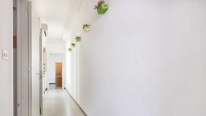 Un couloir aux murs blancs, doté d’un sol carrelé et agrémenté de plusieurs plantes en pot suspendues au plafond.