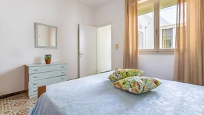 Une chambre à coucher avec un lit, une commode, un miroir et une fenêtre avec des rideaux.
