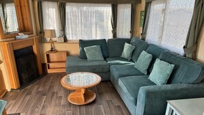 A cozy living area with a sectional sofa, a round wooden coffee table, and a fireplace. - Family Caravan - Sleeps 6 - Pets allowed - Pool (King's Lynn)