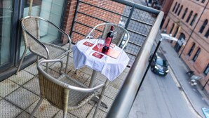 A balcony with wicker chairs, a small table with a bottle and glasses, and a city street view. - Apartment Sleeps 6 with Balcony and Parking (Birmingham)