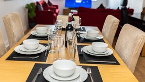 A dining table set with white bowls, glasses, and cutlery, with a bottle of wine and a TV in the background. - Apartment Sleeps 6 with Balcony and Parking (Birmingham)