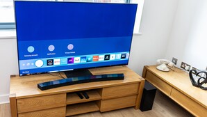 A modern living room with a large flat-screen TV on a wooden stand, a remote control, and a small speaker. - Apartment Sleeps 6 with Balcony and Parking (Birmingham)
