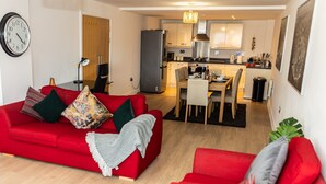 A modern living room with a red sofa, a dining area with a wooden table, and a kitchen with white cabinets and a stainless steel refrigerator. - Apartment Sleeps 6 with Balcony and Parking (Birmingham)