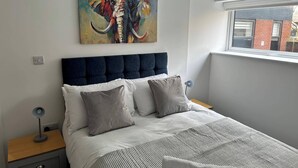 A bedroom with a large bed, a headboard, a nightstand, a lamp, and a painting of an elephant on the wall.