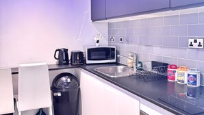 A modern kitchen with white cabinets, a black countertop, a microwave, a kettle, and a trash bin.