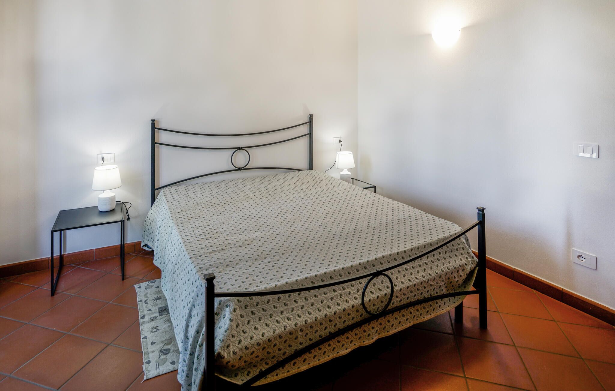 A single bed with a metal frame, two bedside tables with lamps, and a patterned bedspread.