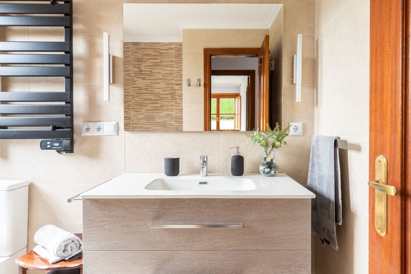Une salle de bain moderne avec un grand miroir, un lavabo, un porte-serviettes et un meuble en bois.