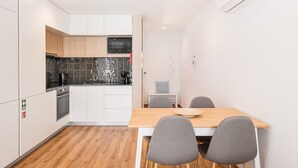 Een compacte keuken met witte kasten, een zwarte magnetron en een houten eettafel met vier grijze stoelen.